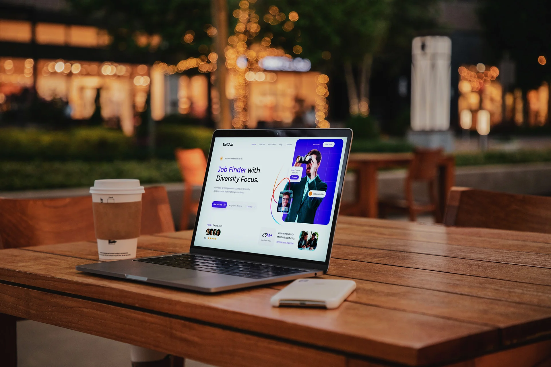 A business owner's laptop on a table at a busy cafe. The screen shows a website design by Digital Den