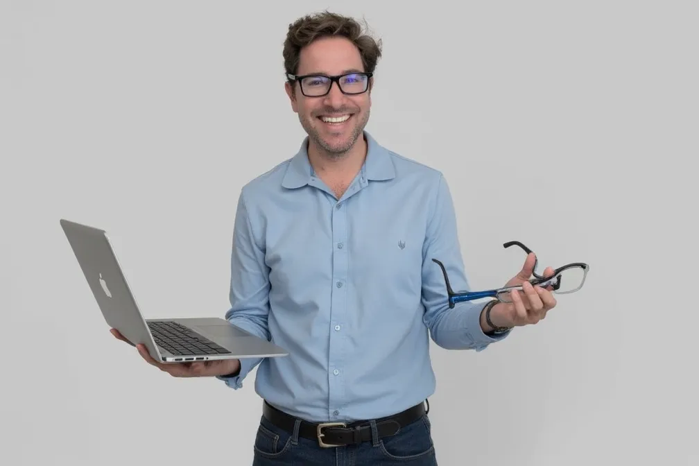 Lee Stoka your tech guy is smiling at the camera and holding a laptop and a pair of glasses
